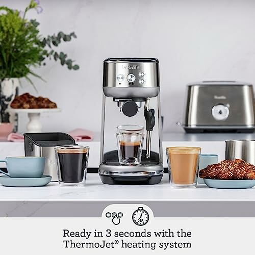 Espresso machine on kitchen counter with cups and pastries.